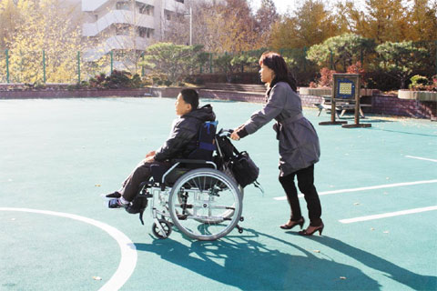 류정화 기자(오른쪽)가 뇌병변 1급 장애아 동준이(가명)의 휠체어를 밀며 이동을 보조하고 있다. 낮은 턱도 동준이와 류 기자에게는 큰 장애물이었다.