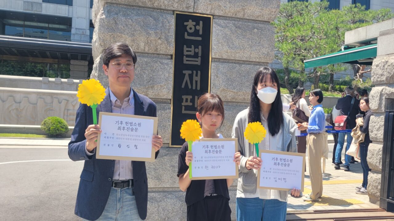 (왼쪽부터) 최종 진술을 맡은 황인철 시민기후소송 청구인· 한제아 아기기후소송 청구인·김서경 청소년기후소송 청구인이 기후 헌법소원 두 번째 공개변론일인 5월 21일 서울 종로구 헌법재판소 앞에서 최후 진술문과 메리골드 종이꽃을 손에 들고 있다. /채예빈 기자